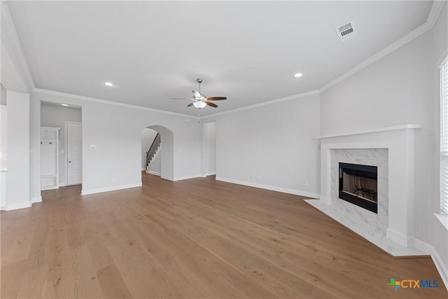 unfurnished living room with ceiling fan, a premium fireplace, ornamental molding, and light hardwood / wood-style flooring