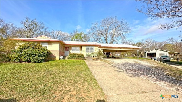 single story home featuring an outbuilding, an attached carport, driveway, and a front lawn
