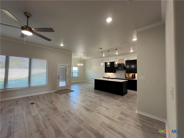 kitchen featuring decorative backsplash, ceiling fan, crown molding, light hardwood / wood-style floors, and an island with sink