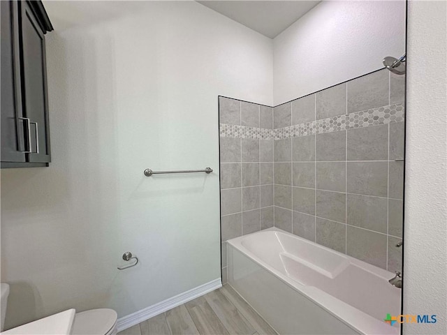 bathroom featuring wood-type flooring, tiled shower / bath combo, and toilet