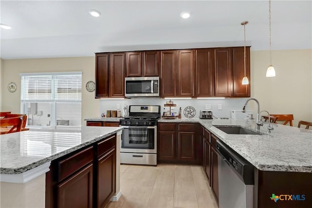 kitchen with light stone counters, a peninsula, stainless steel appliances, a sink, and recessed lighting