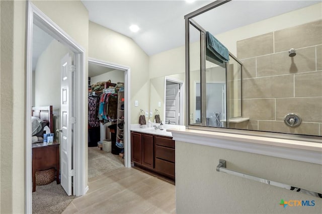 bathroom with lofted ceiling, a tile shower, vanity, and a spacious closet