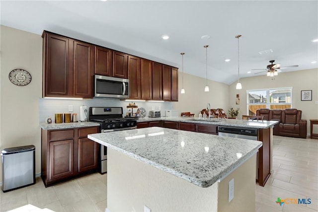 kitchen with light stone counters, a center island, stainless steel appliances, a sink, and a peninsula