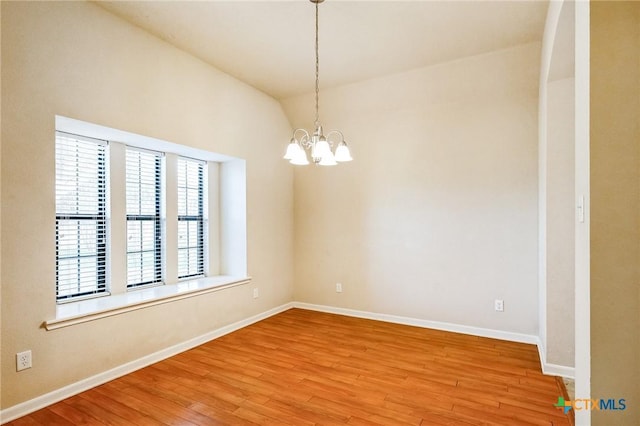 spare room featuring an inviting chandelier, vaulted ceiling, and light wood-type flooring