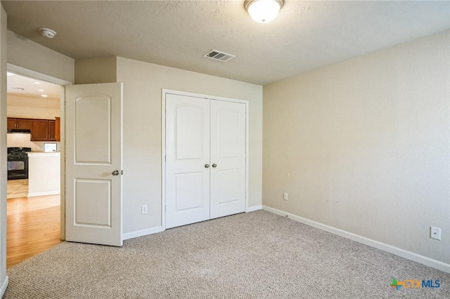 unfurnished bedroom featuring light carpet, a textured ceiling, and a closet