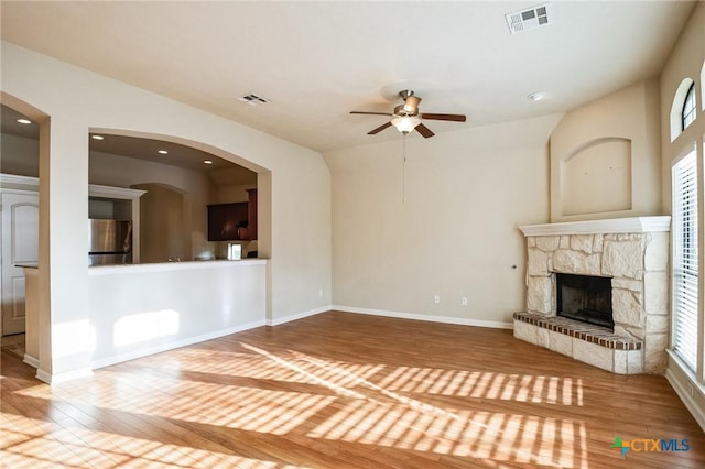 unfurnished living room featuring hardwood / wood-style flooring, ceiling fan, and a stone fireplace