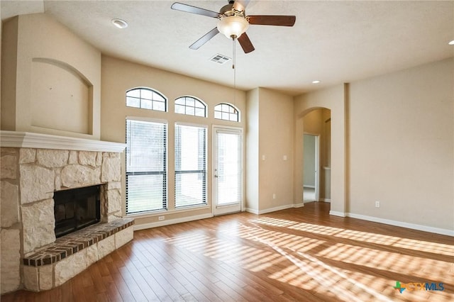 unfurnished living room featuring wood-type flooring, a stone fireplace, and ceiling fan