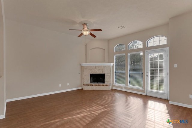 unfurnished living room with hardwood / wood-style flooring, a stone fireplace, and ceiling fan