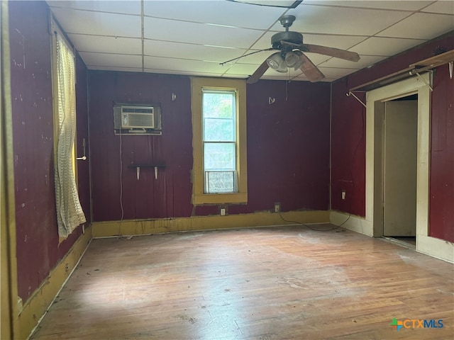 interior space featuring a drop ceiling, hardwood / wood-style floors, an AC wall unit, and ceiling fan