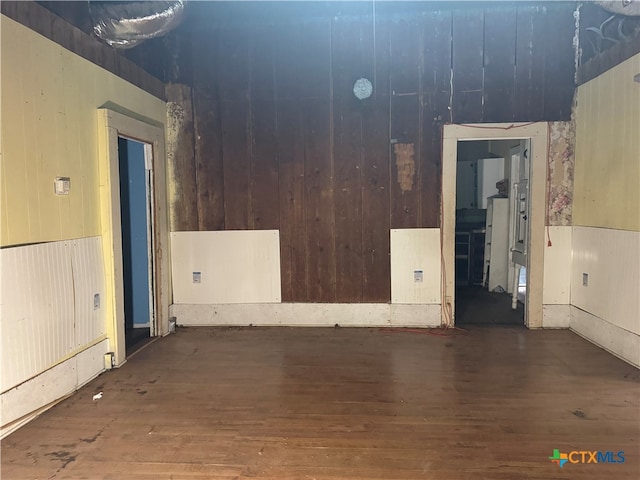 spare room featuring wood walls and dark wood-type flooring