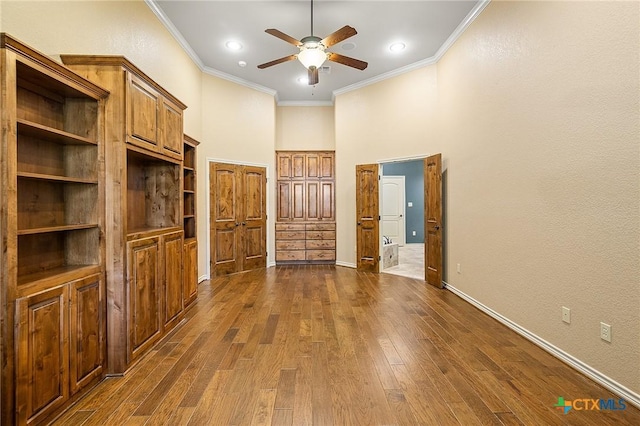 interior space with dark wood-type flooring, ceiling fan, ornamental molding, and a high ceiling