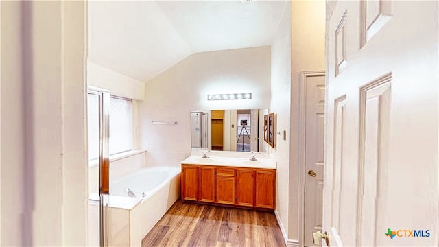 bathroom featuring vanity, wood-type flooring, a tub, and vaulted ceiling