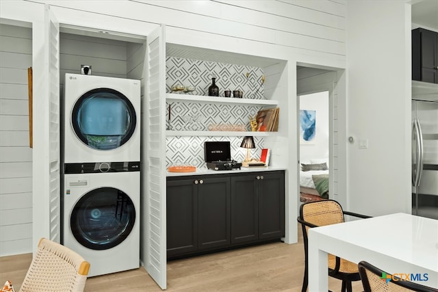 clothes washing area with light hardwood / wood-style flooring, wood walls, and stacked washer and clothes dryer