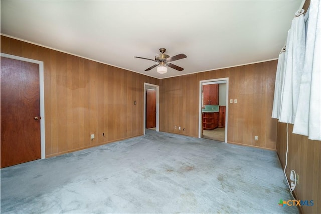 unfurnished bedroom with light colored carpet, ensuite bath, wooden walls, and a ceiling fan