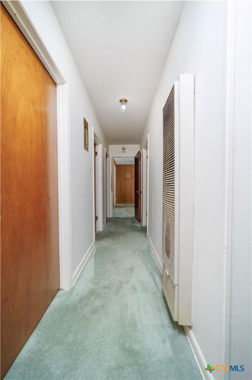 hallway featuring light colored carpet, baseboards, and a heating unit