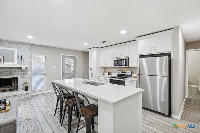 kitchen with appliances with stainless steel finishes, a kitchen island with sink, sink, white cabinetry, and a breakfast bar area