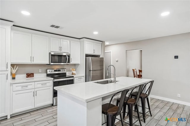 kitchen with a kitchen breakfast bar, sink, an island with sink, white cabinetry, and stainless steel appliances