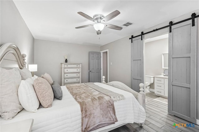 bedroom with connected bathroom, a barn door, ceiling fan, and light hardwood / wood-style floors