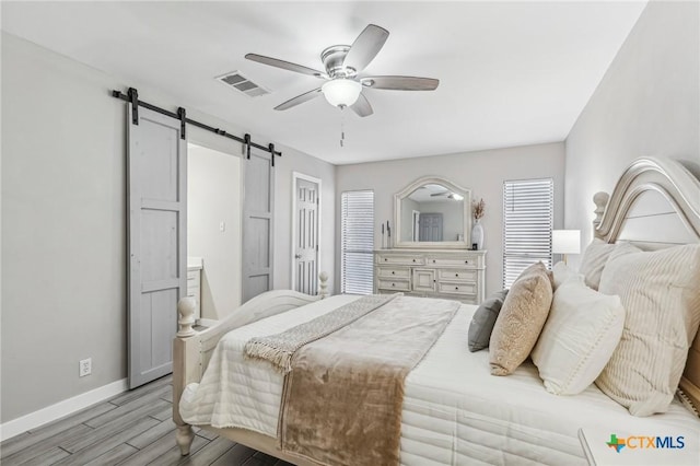 bedroom featuring a barn door, ceiling fan, and light wood-type flooring