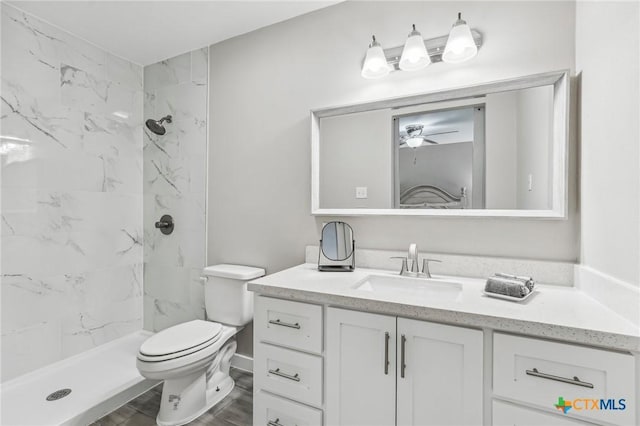 bathroom featuring a tile shower, ceiling fan, vanity, and toilet