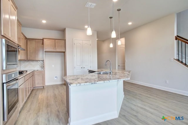 kitchen with appliances with stainless steel finishes, sink, backsplash, a kitchen island with sink, and light stone counters