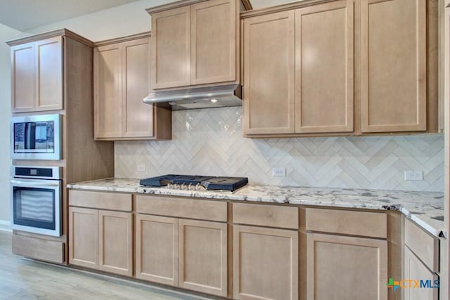 kitchen featuring appliances with stainless steel finishes, decorative backsplash, light wood-type flooring, light stone counters, and light brown cabinets