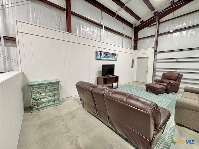 living room featuring wood walls, beamed ceiling, a towering ceiling, and concrete flooring