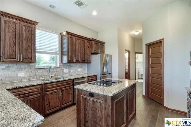 kitchen featuring sink, light stone counters, appliances with stainless steel finishes, dark hardwood / wood-style floors, and a center island