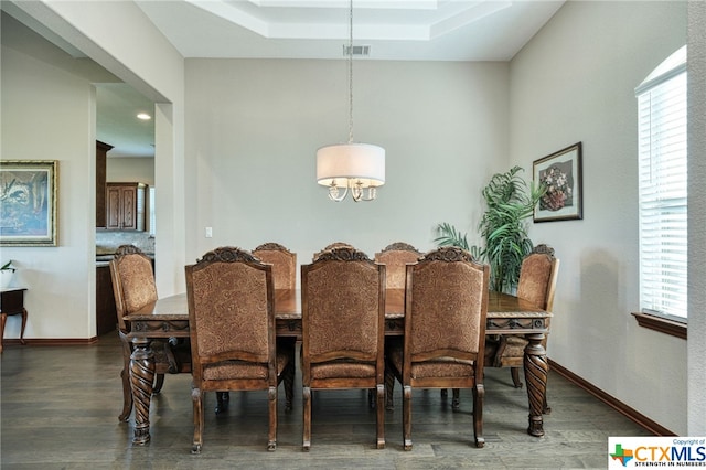 dining area with dark hardwood / wood-style floors and a raised ceiling