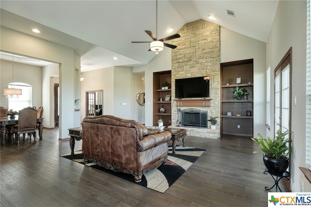 living room with built in shelves, a stone fireplace, dark hardwood / wood-style floors, and plenty of natural light