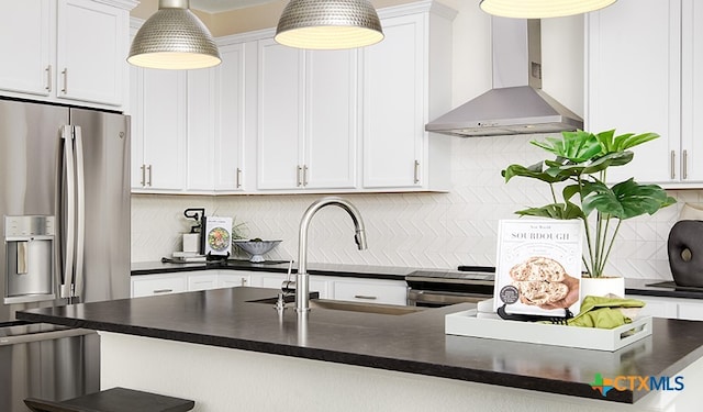 kitchen with tasteful backsplash, white cabinetry, wall chimney range hood, appliances with stainless steel finishes, and decorative light fixtures