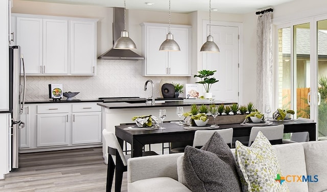 kitchen with pendant lighting, white cabinetry, wall chimney exhaust hood, and stainless steel refrigerator