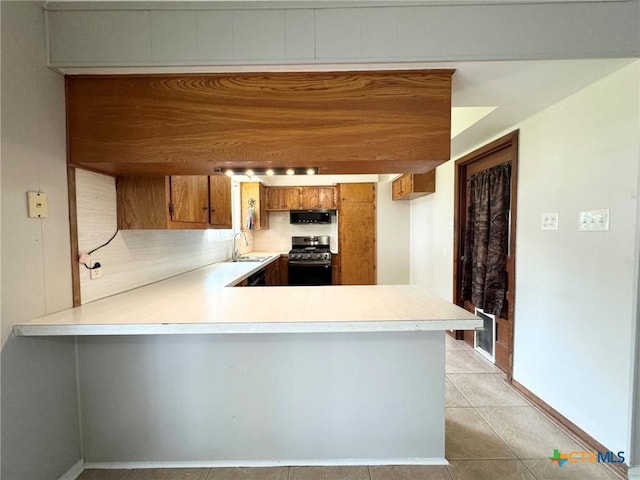 kitchen with light tile patterned floors, sink, stainless steel range oven, and kitchen peninsula