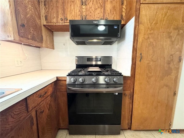 kitchen featuring stainless steel gas stove, light tile patterned floors, and decorative backsplash