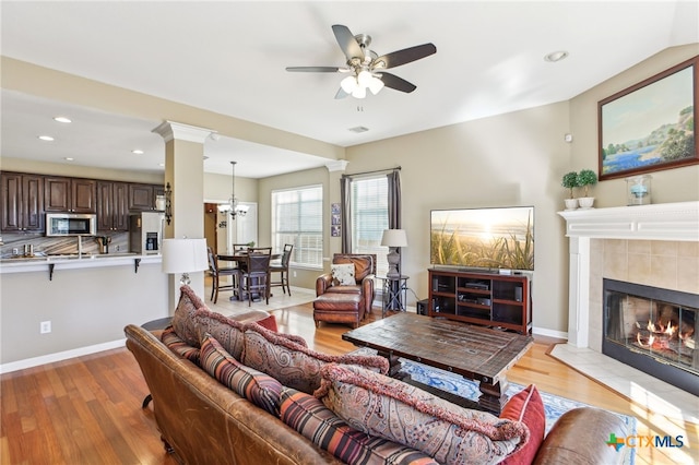 living room with decorative columns, a tile fireplace, ceiling fan with notable chandelier, and light hardwood / wood-style flooring