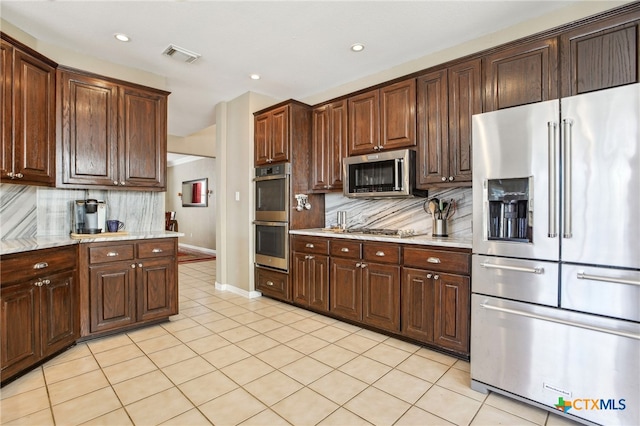 kitchen with backsplash, stainless steel appliances, light stone countertops, and light tile patterned floors