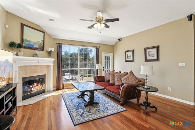 living room with vaulted ceiling, light hardwood / wood-style floors, a tile fireplace, and ceiling fan