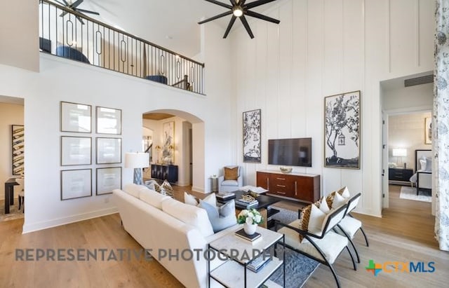 living room featuring a towering ceiling, light hardwood / wood-style floors, and ceiling fan