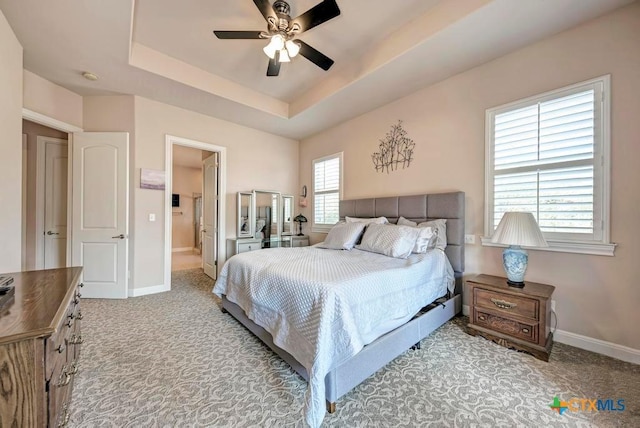 carpeted bedroom featuring a ceiling fan, a raised ceiling, and baseboards