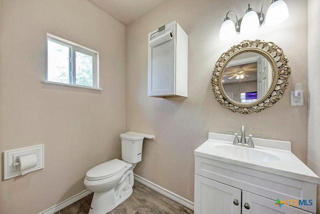 half bathroom with baseboards, vanity, toilet, and wood finished floors