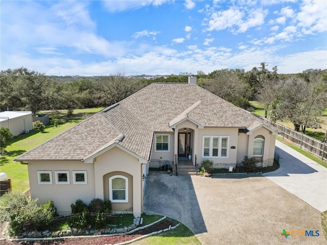 view of front facade with driveway, a shingled roof, fence, and stucco siding