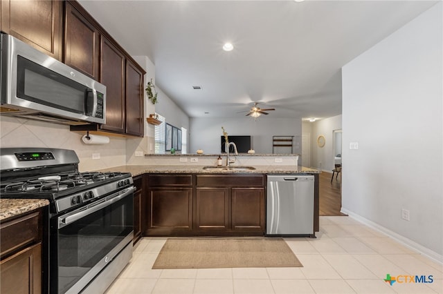 kitchen with dark brown cabinets, appliances with stainless steel finishes, light stone countertops, and a sink