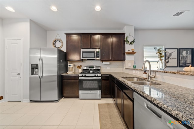 kitchen featuring stone counters, a sink, decorative backsplash, dark brown cabinetry, and stainless steel appliances