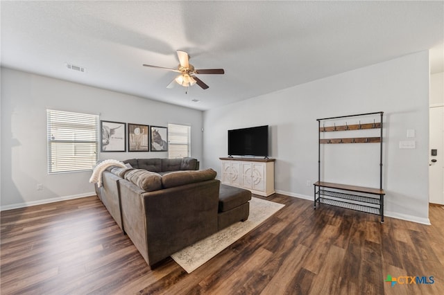 living area featuring visible vents, baseboards, dark wood finished floors, and a ceiling fan