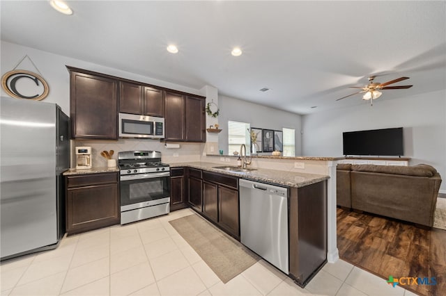 kitchen featuring light stone countertops, dark brown cabinetry, a peninsula, stainless steel appliances, and a sink