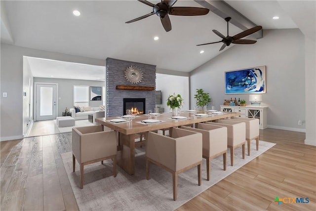 dining room with beamed ceiling, high vaulted ceiling, a fireplace, and light hardwood / wood-style flooring