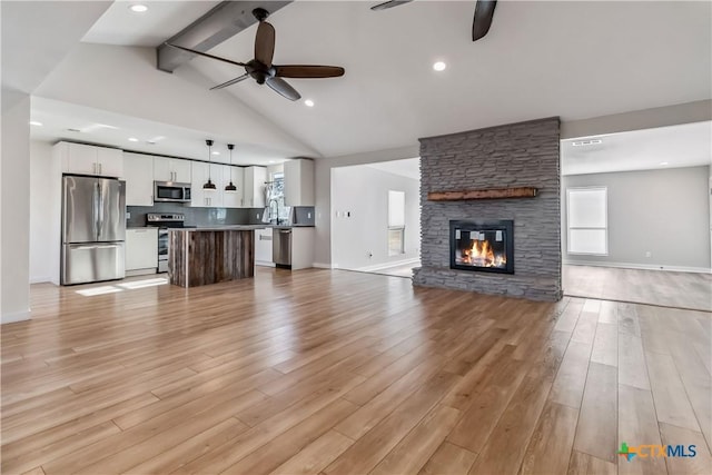 unfurnished living room with high vaulted ceiling, a fireplace, light wood-type flooring, ceiling fan, and beam ceiling