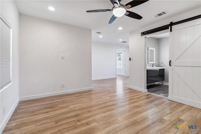 spare room featuring ceiling fan, a barn door, and light wood-type flooring