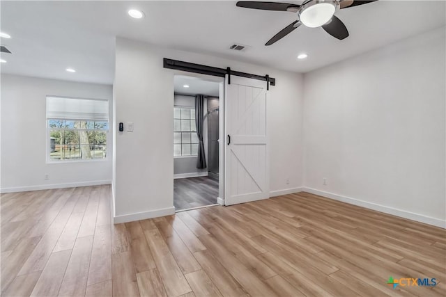 unfurnished bedroom featuring ceiling fan, a barn door, light wood-type flooring, and ensuite bath