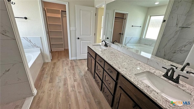 bathroom with a bath, double vanity, a sink, and wood finished floors